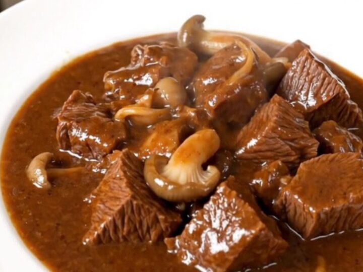 A close-up of a slow cooker beef stew with tender beef cubes and pleurotus mushrooms in a rich red wine sauce.