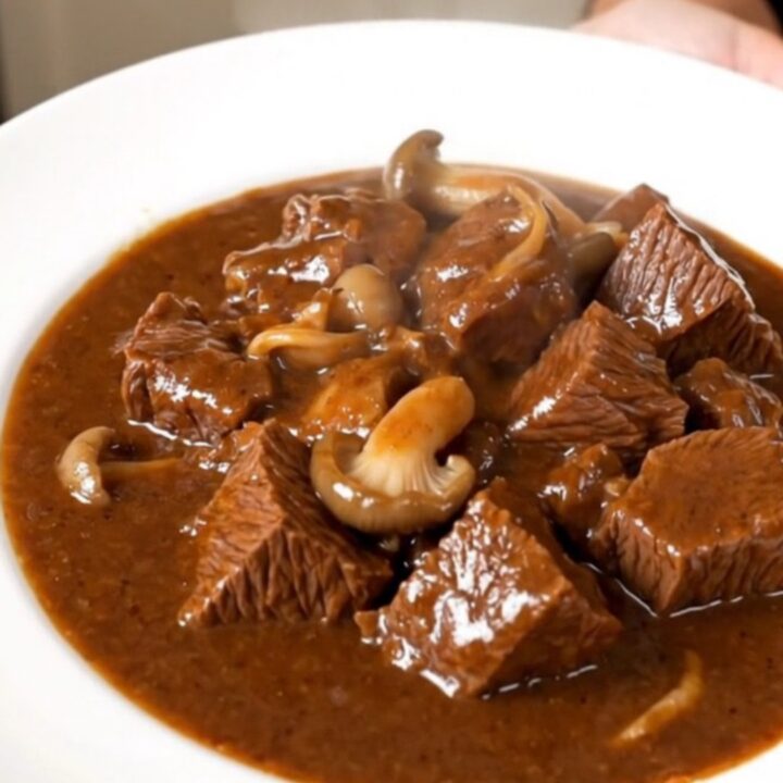 A close-up of a slow cooker beef stew with tender beef cubes and pleurotus mushrooms in a rich red wine sauce.