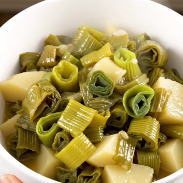 A white bowl filled with glossy, tender leeks and diced potatoes in a light, savory broth.