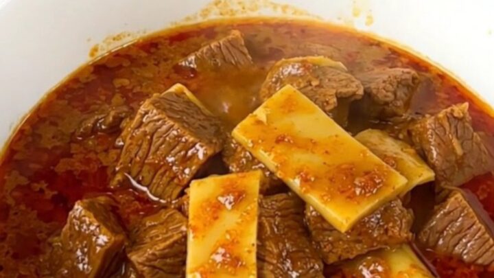 Un curry thaï au bœuf et lait de coco servi dans un bol blanc sur un plan de travail.