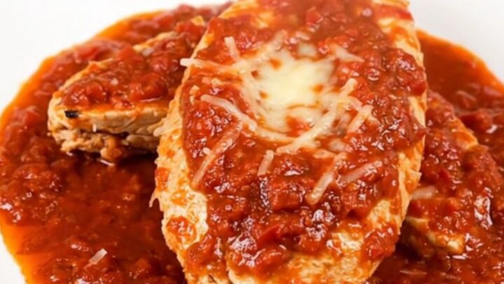 A top-down view of a slow cooker filled with chicken fillets, crushed tomatoes, and broth before cooking.