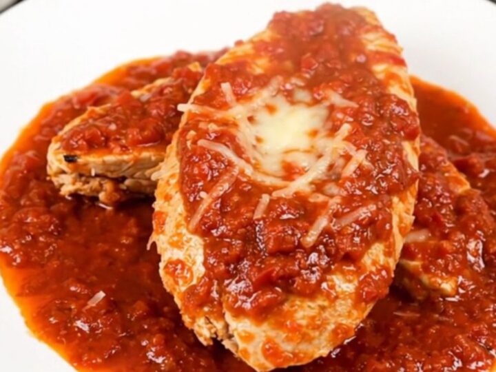 A top-down view of a slow cooker filled with chicken fillets, crushed tomatoes, and broth before cooking.