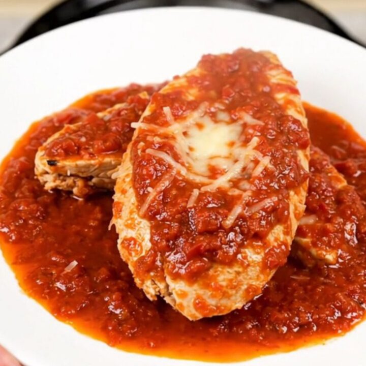 A top-down view of a slow cooker filled with chicken fillets, crushed tomatoes, and broth before cooking.