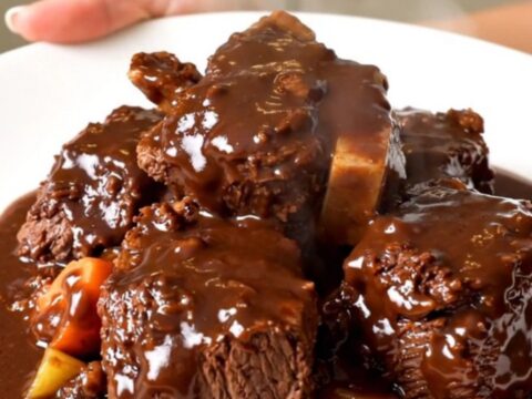 A close-up of slow cooker beef bourguignon with glossy sauce on a white plate.
