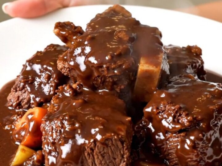 A close-up of slow cooker beef bourguignon with glossy sauce on a white plate.