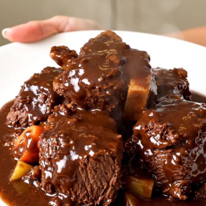 A close-up of slow cooker beef bourguignon with glossy sauce on a white plate.