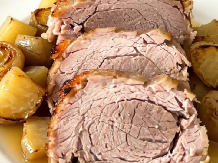 A tender, slow-cooked pork roast served on a white plate with glossy, cooked parsnips and carrots.