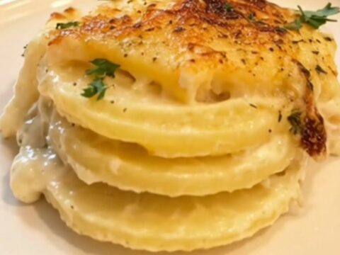 A golden, bubbling roasted garlic potato gratin served in a glass dish with fresh parsley.