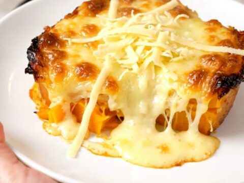 A creamy butternut squash gratin in a black slow cooker, topped with melted golden Emmental cheese.