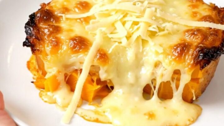 A creamy butternut squash gratin in a black slow cooker, topped with melted golden Emmental cheese.