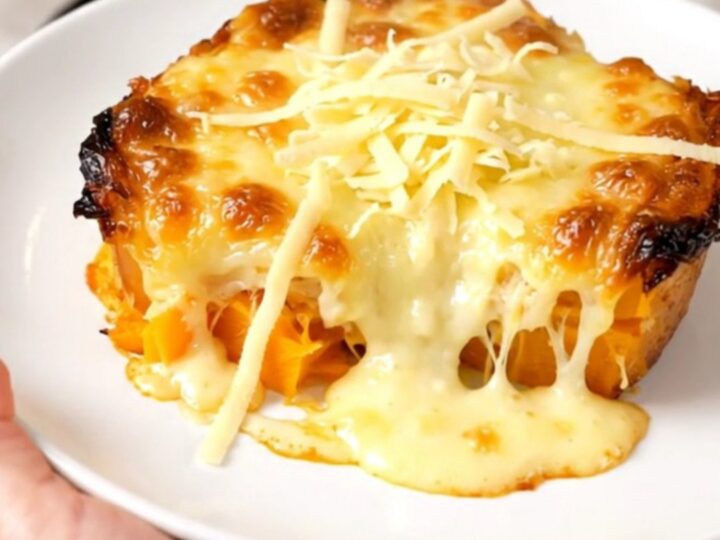 A creamy butternut squash gratin in a black slow cooker, topped with melted golden Emmental cheese.