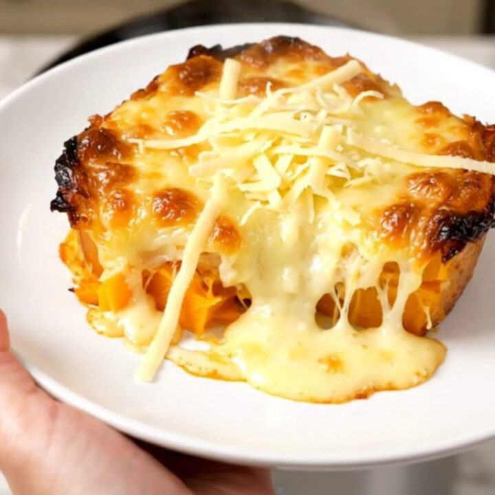 A creamy butternut squash gratin in a black slow cooker, topped with melted golden Emmental cheese.