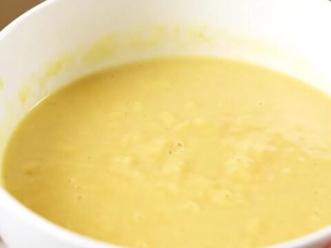 A steaming bowl of silky, pale yellow parsnip and carrot soup served in a white ceramic bowl.