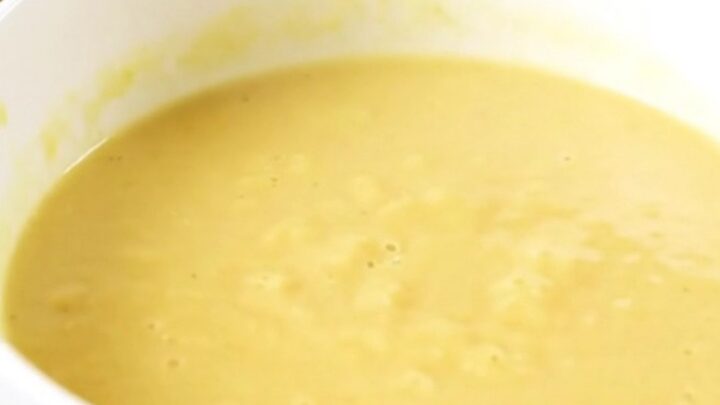 A steaming bowl of silky, pale yellow parsnip and carrot soup served in a white ceramic bowl.