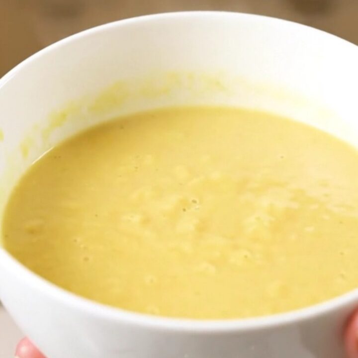 A steaming bowl of silky, pale yellow parsnip and carrot soup served in a white ceramic bowl.
