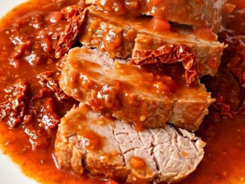 A slow cooker filled with a cooked pork tenderloin, sun-dried tomatoes, and a rich, glossy tomato and basil sauce.