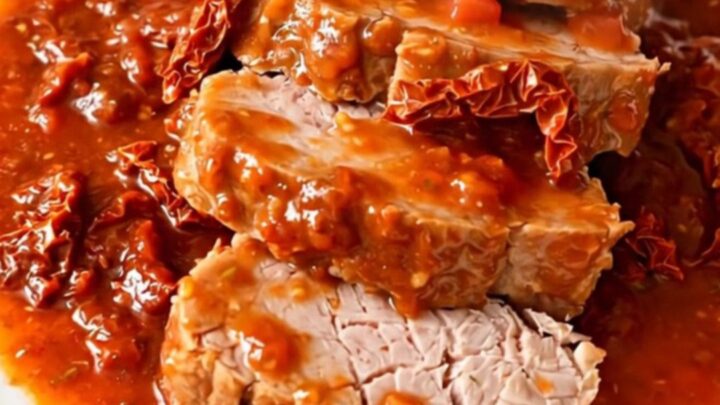 A slow cooker filled with a cooked pork tenderloin, sun-dried tomatoes, and a rich, glossy tomato and basil sauce.