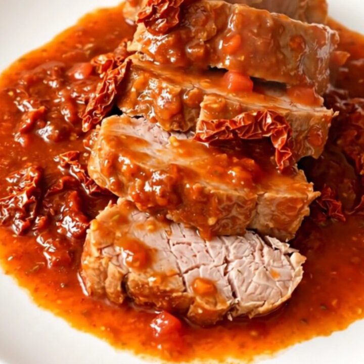 A slow cooker filled with a cooked pork tenderloin, sun-dried tomatoes, and a rich, glossy tomato and basil sauce.