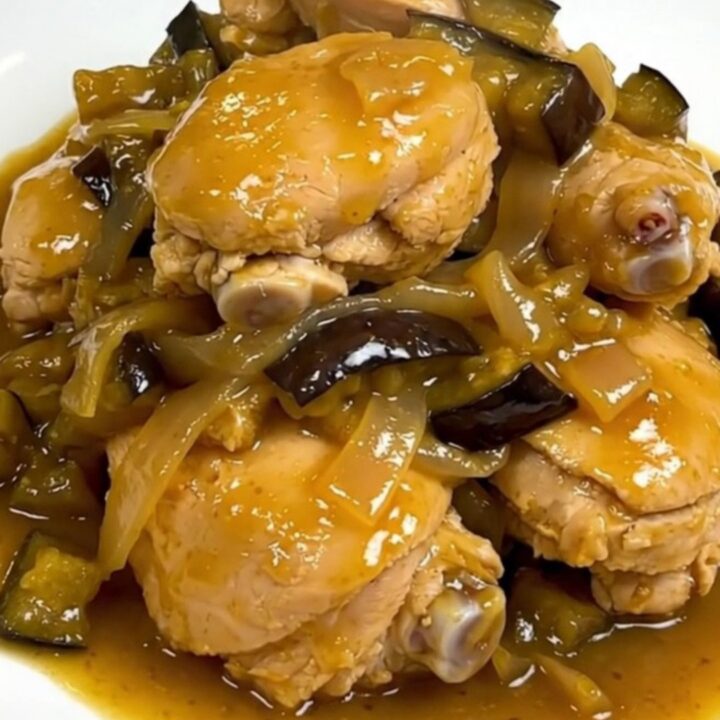 A steaming, glossy chicken and eggplant colombo served on a plain white round plate.