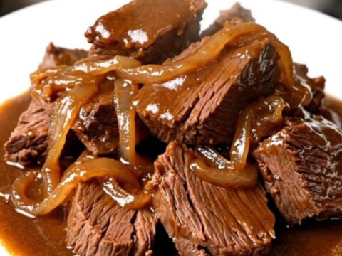 A close-up of tender, glossy amber beer braised beef served on a white plate.