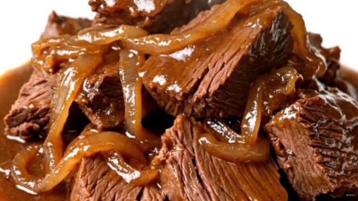 A close-up of tender, glossy amber beer braised beef served on a white plate.
