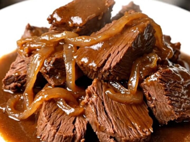 A close-up of tender, glossy amber beer braised beef served on a white plate.