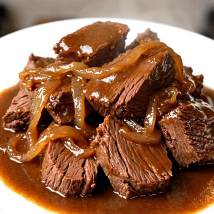 A close-up of tender, glossy amber beer braised beef served on a white plate.