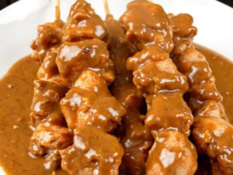 A top-down view of creamy coconut chicken satay in a slow cooker on a white countertop.