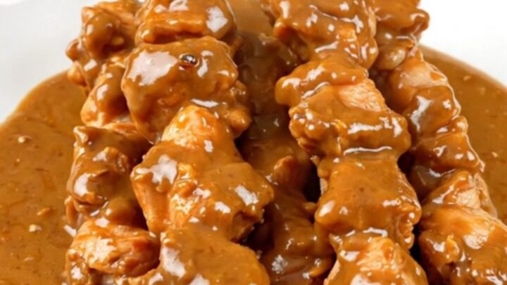 A top-down view of creamy coconut chicken satay in a slow cooker on a white countertop.