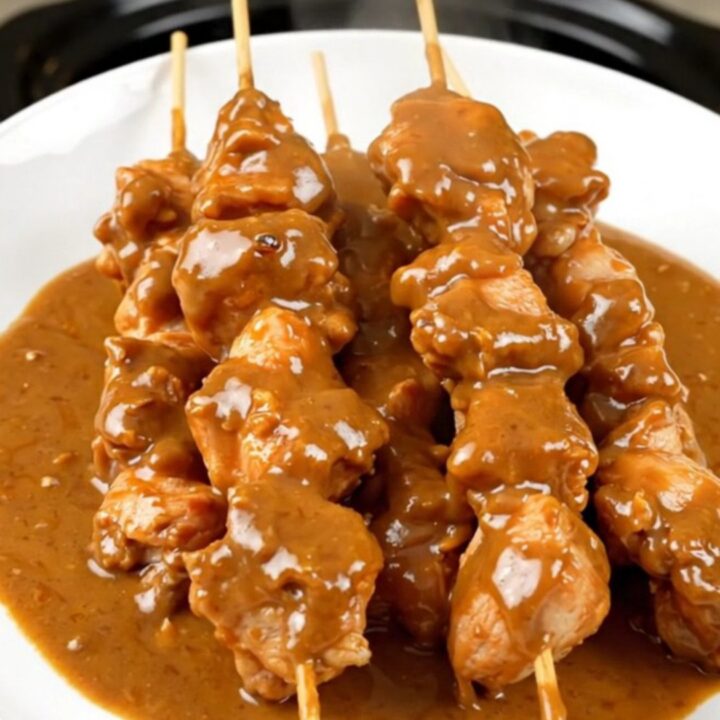 A top-down view of creamy coconut chicken satay in a slow cooker on a white countertop.