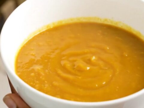 A bowl of velvety orange pumpkin soup sitting on a table with soft kitchen lighting.