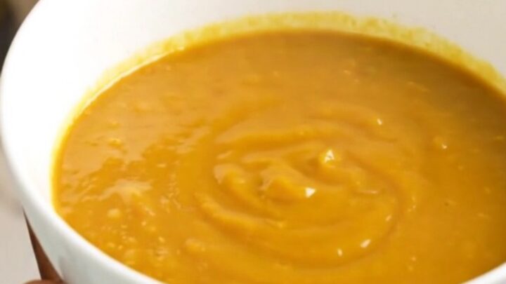 A bowl of velvety orange pumpkin soup sitting on a table with soft kitchen lighting.