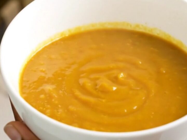 A bowl of velvety orange pumpkin soup sitting on a table with soft kitchen lighting.
