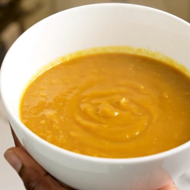 A bowl of velvety orange pumpkin soup sitting on a table with soft kitchen lighting.