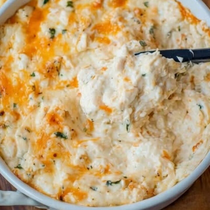 A white ceramic dish filled with golden, bubbling hot crab dip with visible lumps of crab meat.