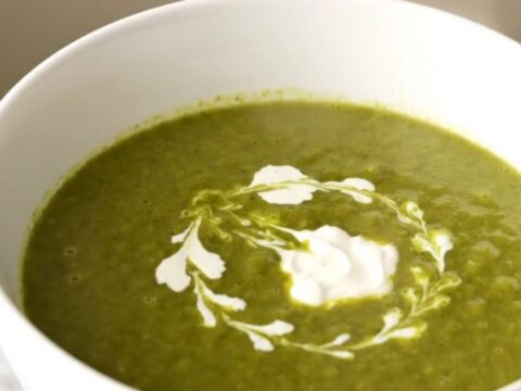 Un bol blanc rempli de velouté de cresson vert vif, décoré d'un filet de crème fraîche sur le dessus.