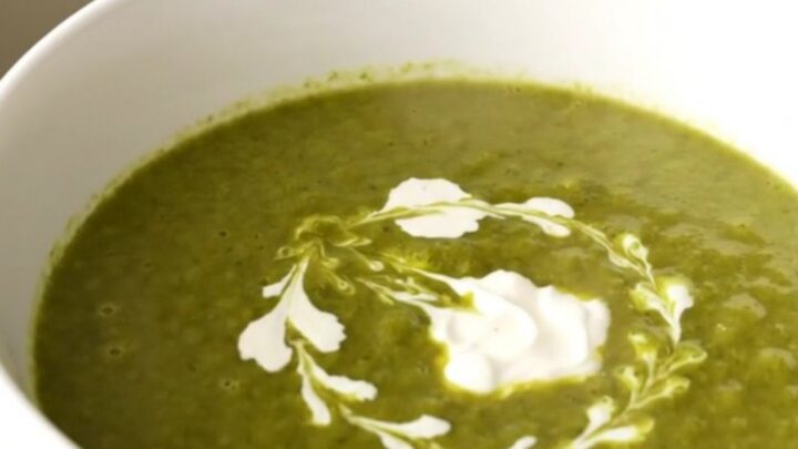 Un bol blanc rempli de velouté de cresson vert vif, décoré d'un filet de crème fraîche sur le dessus.