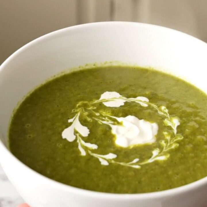 Un bol blanc rempli de velouté de cresson vert vif, décoré d'un filet de crème fraîche sur le dessus.