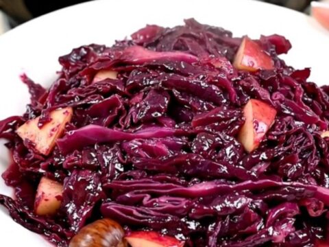Vue de dessus d'un chou rouge braisé aux pommes et marrons dans une mijoteuse noire.