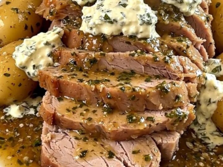 A slow cooker garlic and herb pork roast with baby potatoes and onions served on a white plate.