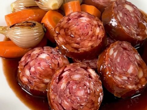 Saucisson lyonnais tranché nappé de sauce au vin rouge brillant avec des morceaux de carottes et d'échalotes.
