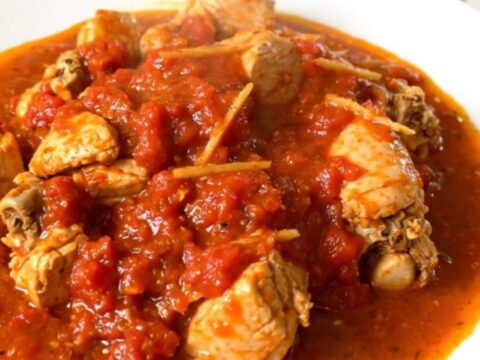 A close-up shot of slow-cooked chicken rougail in a tomato sauce on a white plate.