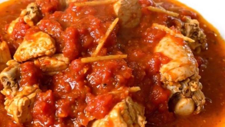A close-up shot of slow-cooked chicken rougail in a tomato sauce on a white plate.