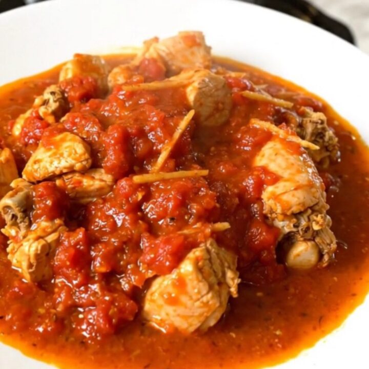 A close-up shot of slow-cooked chicken rougail in a tomato sauce on a white plate.