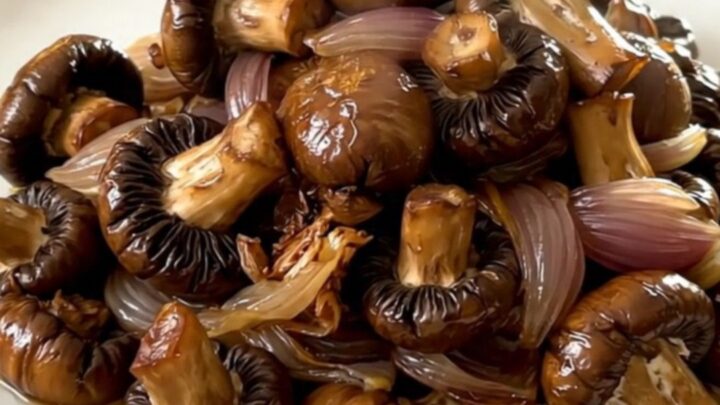 A close-up view of glossy, slow-cooked mushrooms in a cider glaze on a round white plate.