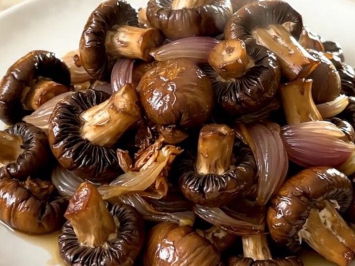 A close-up view of glossy, slow-cooked mushrooms in a cider glaze on a round white plate.