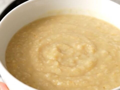 A white bowl filled with creamy, smooth endive and potato soup, steaming gently against a soft-focus kitchen background.