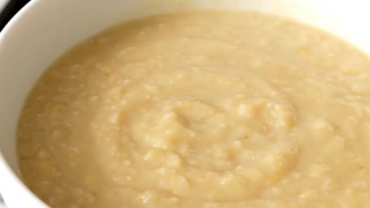 A white bowl filled with creamy, smooth endive and potato soup, steaming gently against a soft-focus kitchen background.