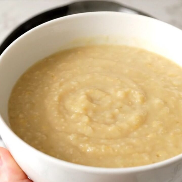 A white bowl filled with creamy, smooth endive and potato soup, steaming gently against a soft-focus kitchen background.