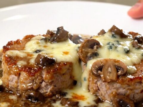 A close-up of creamy blue cheese pork tenderloin medallions on a white plate.